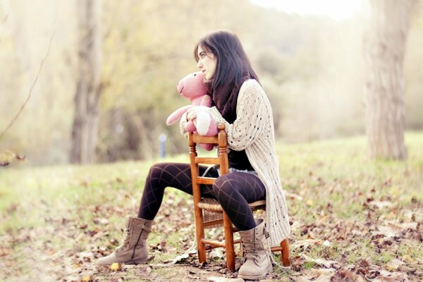 A girl is sitting on a chair with a toy in autumn