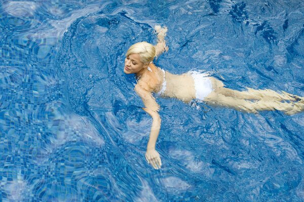 A blonde girl in a white swimsuit swims in the water