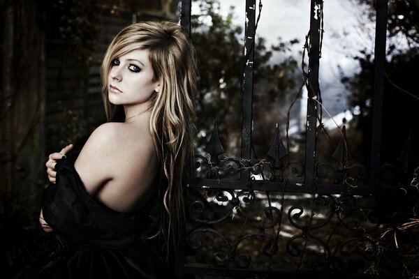 Singer Avril lavigne with long hair in a dark dress poses in a half-turn