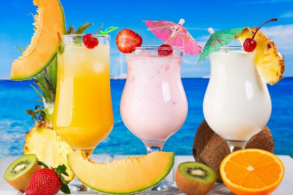 Three cocktails and fruit on the background of the ocean