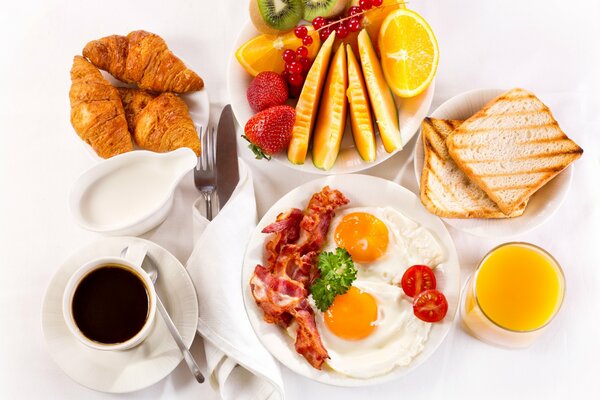 Colazione servita sul tavolo con croissant caffè uova strapazzate con pancetta e frutta