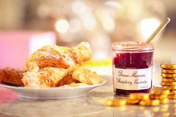 Pastries in a plate on the table and a jar of jam next to it