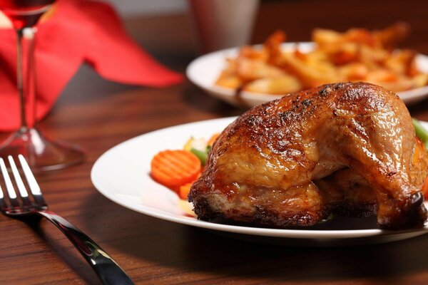 Sul tavolo c è un piatto di pollo e una forchetta con un bicchiere accanto