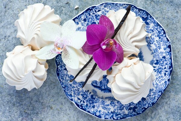 Sweet dessert of white marshmallows on a blue plate with a beautiful pink orchid