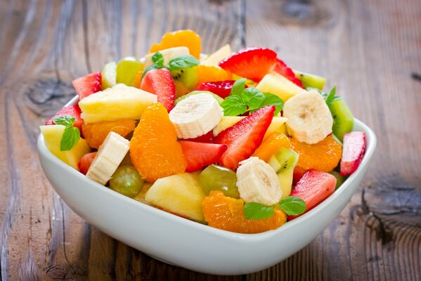 Dessert in Form eines Obstsalats mit Banane, Mandarine, Erdbeeren, Ananas und Minzblättern