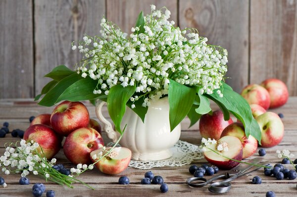 Delicate lilies of the valley on the background of apples and blueberries