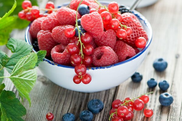 Sur la table se trouve un bol dans lequel se trouvent des fraises, des bleuets, des framboises