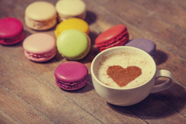 Macarons sur la table à côté du café crémeux dans une tasse avec de la mousse sur laquelle le coeur