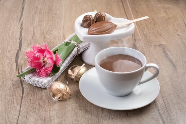 Eine Tasse duftenden Kaffee mit Süßigkeiten und einer Blume