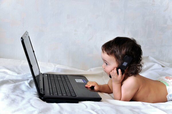 Petit enfant derrière un ordinateur portable avec un téléphone