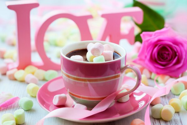 Tasse heiße Schokolade mit Marshmallows auf Rosen-Hintergrund und Love-Schriftzug