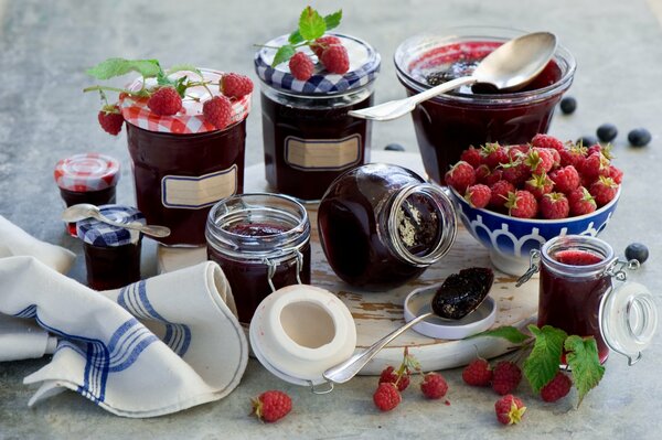 On the table there are jars of jam and a deep plate with raspberries