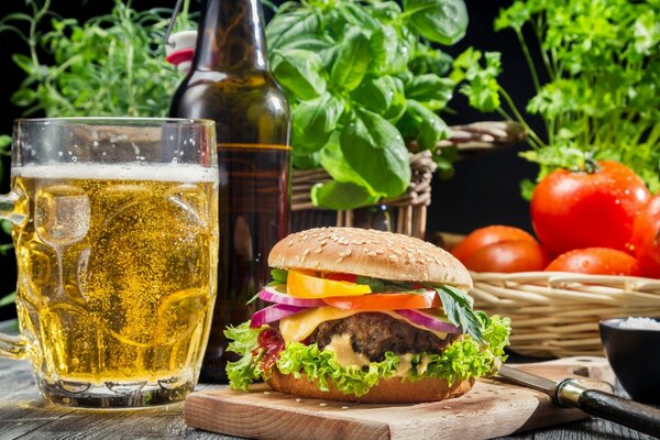 Bicchiere di birra, hamburger, pomodori ed erbe sul tavolo