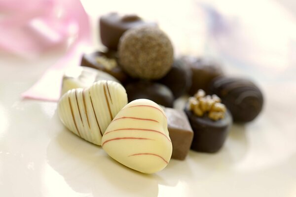 Конфеты в белом шоколаде в виде сердечка на фоне конфет в молочном шоколаде
