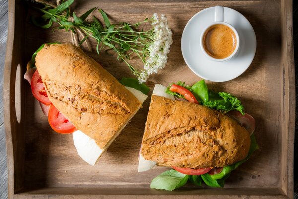 Sandwich mit Kaffee und Blumen in einem Holztablett