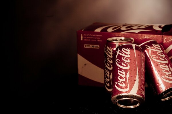 Trois canettes de Coca à côté de la boîte