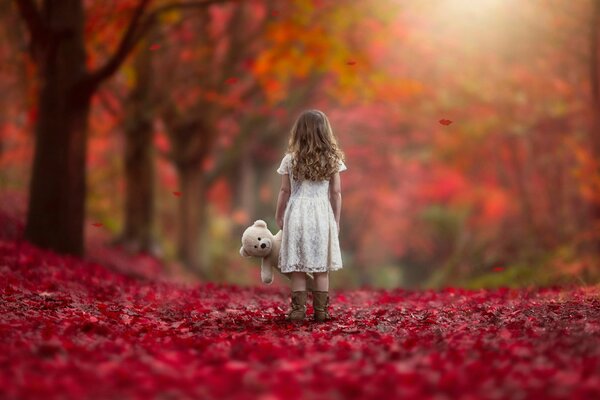 Mädchen mit einem Teddybär auf dem Hintergrund der Herbstlandschaft