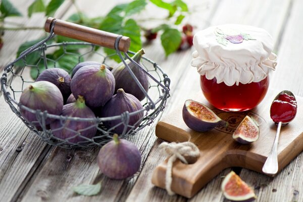 Higos en una canasta junto a un frasco de mermelada en una tabla de madera