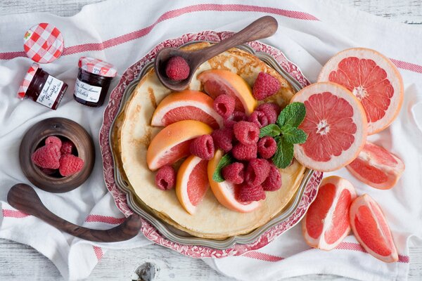 Блинчики с ягодами малины и грейпфрутом на красивой тарелке