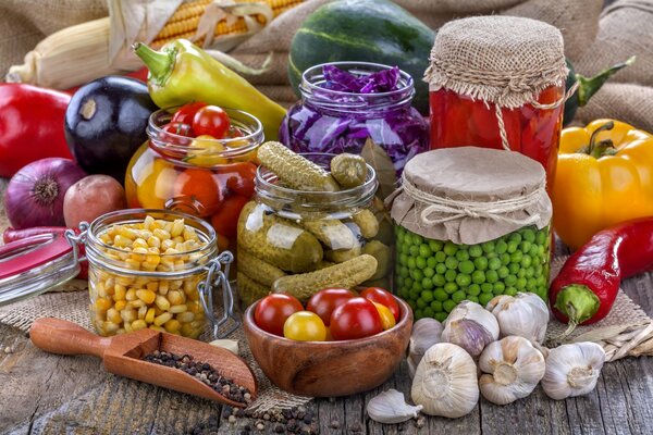 Pepinos enlatados, cebollas, ajo y guisantes en un frasco en una mesa de madera