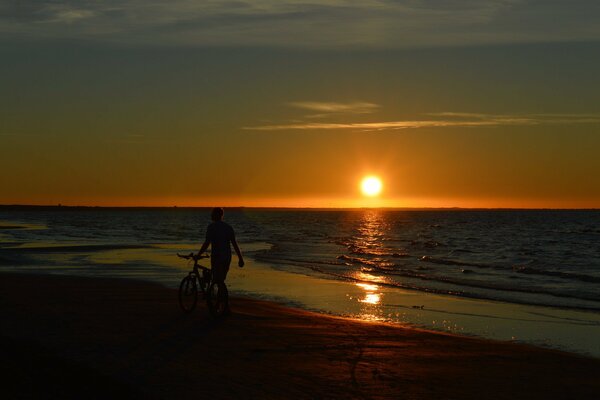 A man walking along the beach against the sunset