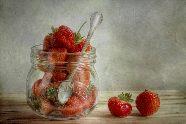 Glass jar with a spoon together with strawberries