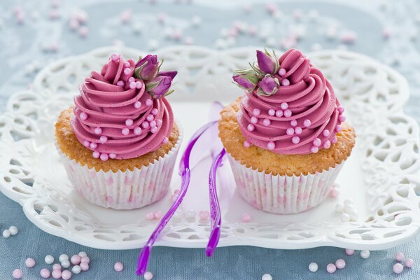 Auf einem weißen Tablett stehen Muffins mit rosa Sahne