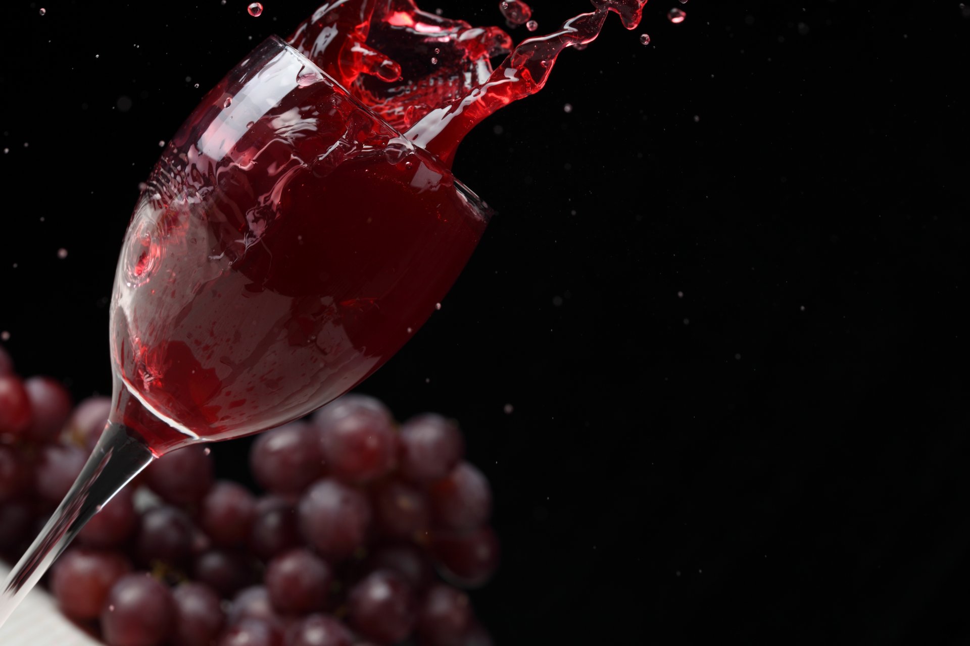 wine red glass spray grapes black background