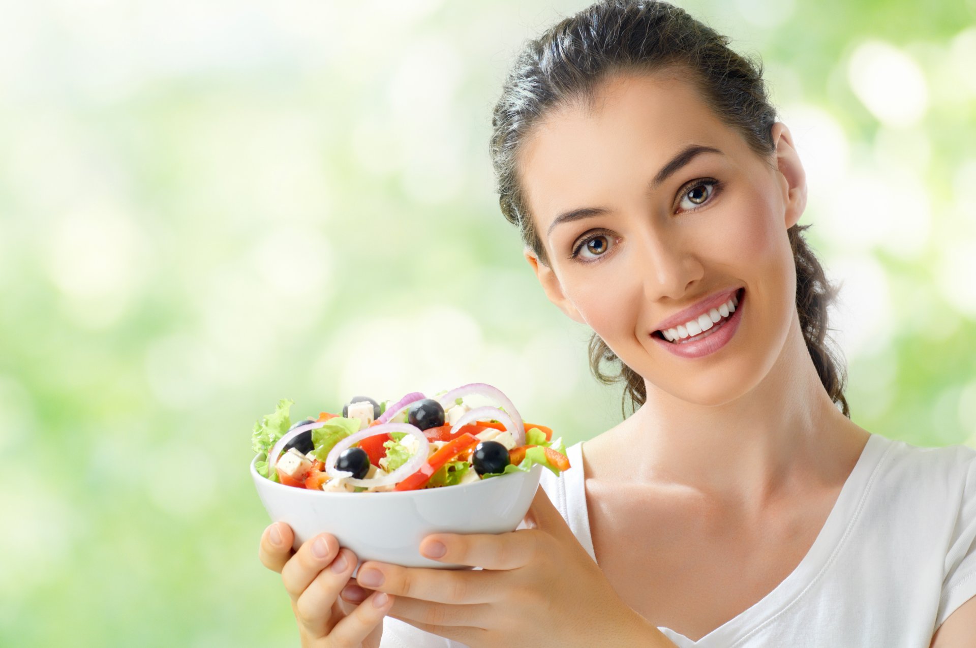 chica morena plato tenedor ensalada verduras encanto pepinos aceitunas cebolla queso tomates camiseta sonrisa bokeh ojos marrones mirada