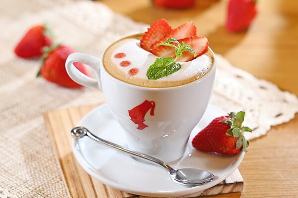 A cup of fragrant cappuccino with strawberries on the table