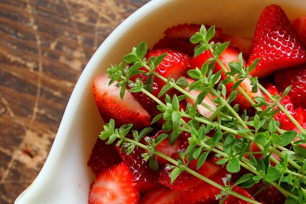 A plate with strawberries and herbs on a wooden table