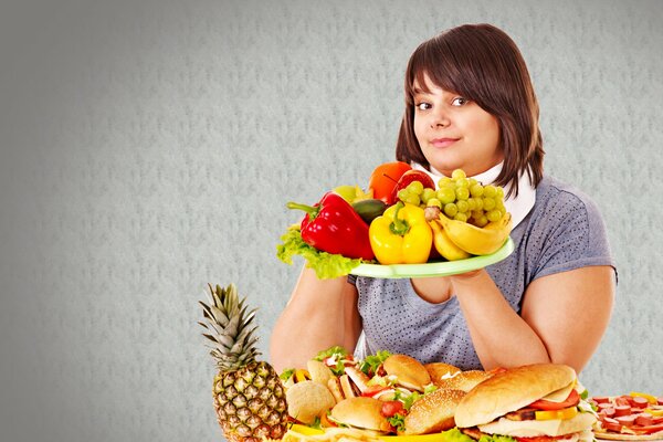 Una chica sostiene una bandeja de fruta. Hamburguesas y sándwiches en la mesa