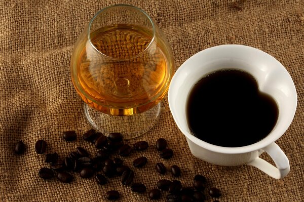 Eine Tasse Kaffee, ein Glas Cognac und zerstreute Kaffeebohnen auf einem Jutetuch