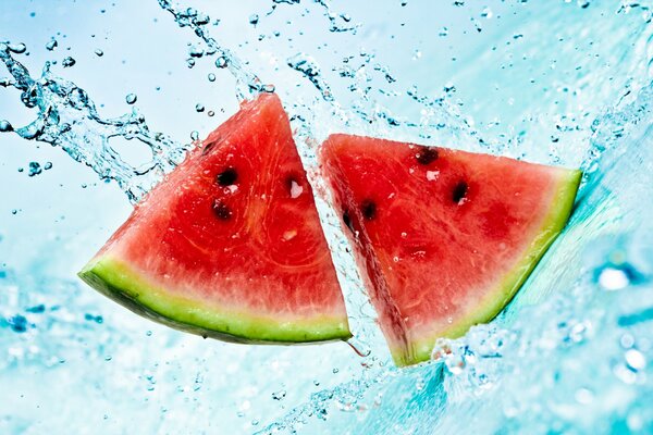 Zwei Stücke Wassermelone fallen mit Spritzwasser ins Wasser