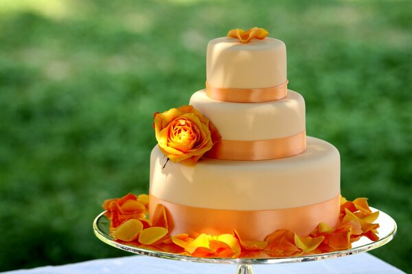 Delicious big cake with orange ribbons, which are decorated with yellow roses and petals
