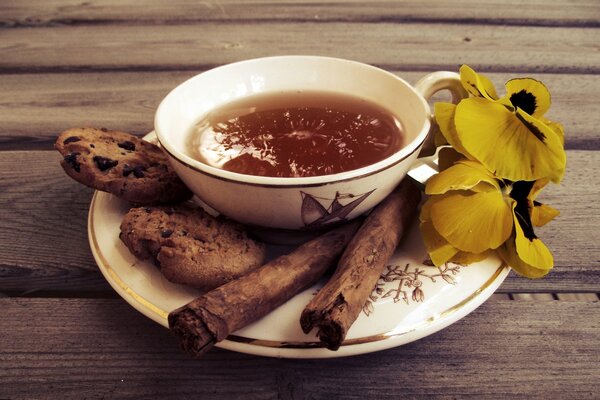 Tazza di tè con biscotti e cannella, fiori su un piattino