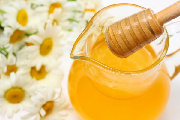Honey with a spoon on the background of daisies