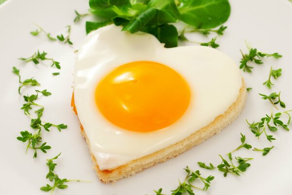 Huevo frito en una tostada en forma de corazón con verduras en un plato