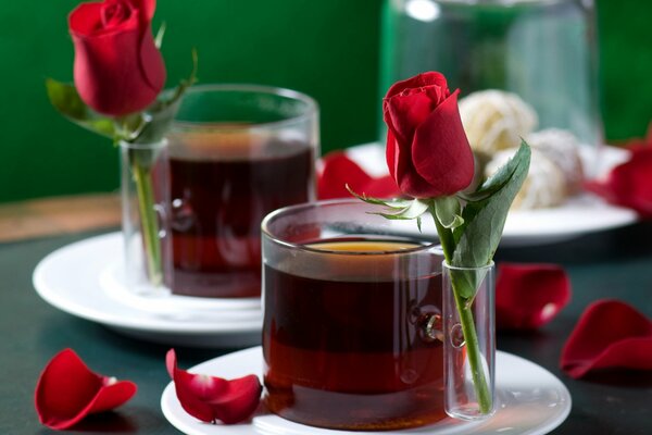 Zwei Tassen Tee auf weißen Untertassen mit roten Rosen und Rosenblättern für einen romantischen Abend eines jungen Paares