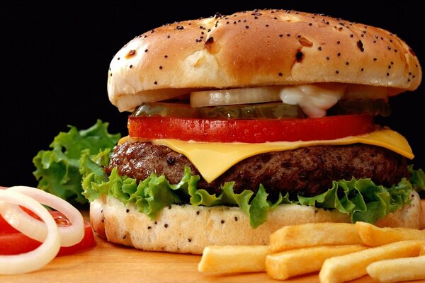 Burger avec escalope, fromage, légumes et légumes verts, glace sur une planche parmi les légumes et les frites