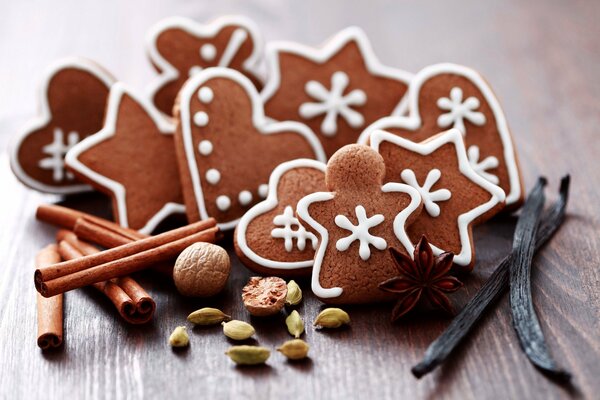 Biscotti di Capodanno a forma di fiocchi di neve, stelle e cuori con bastoncini di cannella e noci su un tavolo di legno
