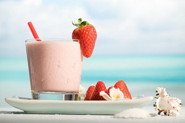 Koktel alla fragola circondato da conchiglie sulla riva del mare