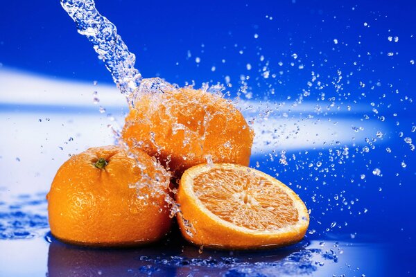 Сочные апельсины в брызгах воды на синем фон