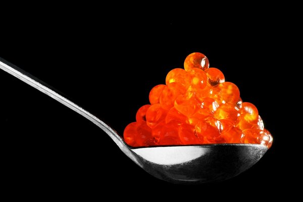 A spoon with red caviar on a black background