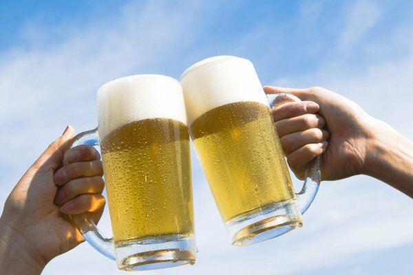 Foamy beer in a mug against the sky