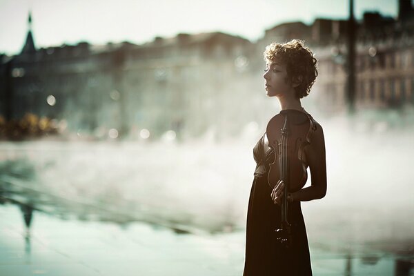 A girl with a violin on a foggy morning