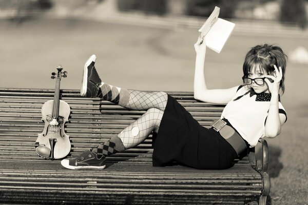The girl is lying on a bench with a violin