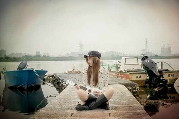 A girl in a cap sitting on the pier