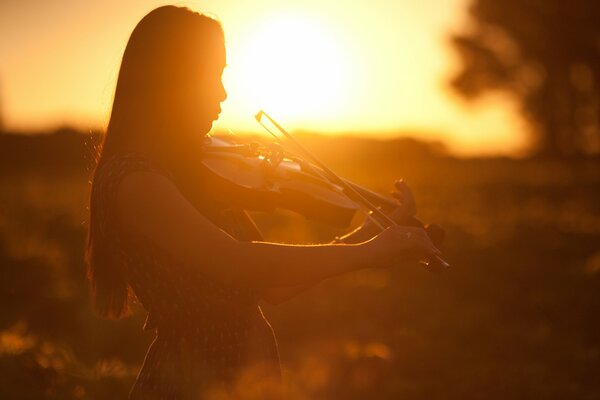 A girl plays the violin in the sunset light