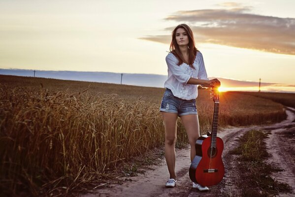 Dziewczyna z gitarą w polu na tle zachodu Słońca